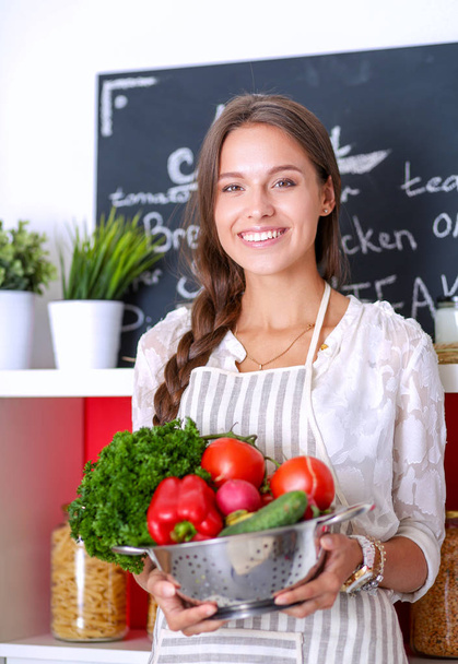 Smiling young woman holding vegetables standing in kitchen. Smiling young woman - Photo, Image
