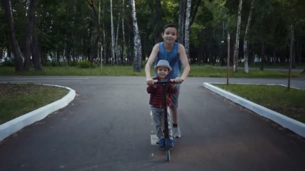 夏の公園のキック スクーターに乗って二人の兄弟. - 映像、動画