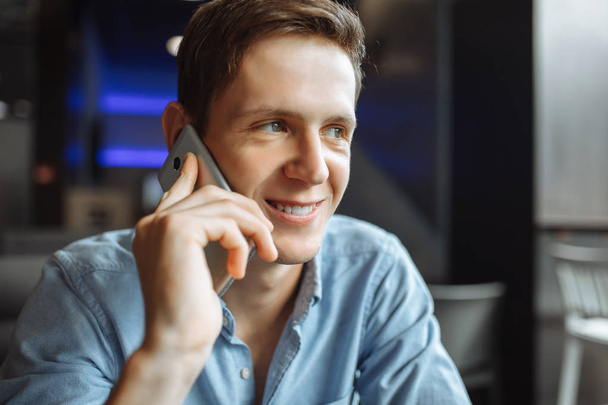 Happy young man, emotionally talking on the phone, sitting in a cafe, - 写真・画像