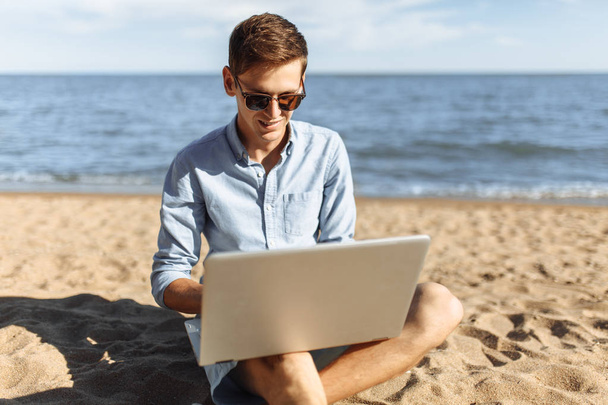 Young guy with glasses, working on his laptop on the beach, work on vacation, - Photo, image
