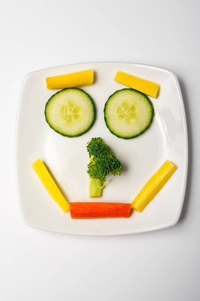 Smiley-Gesicht aus Gemüse zeigt glückliche gesunde Ernährung auf weißem Teller. - Foto, Bild