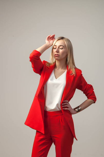 Young beautiful white blond girl in a bright red strict suit with a jacket and white blouse standing in a pose on a white isolated background - Fotó, kép