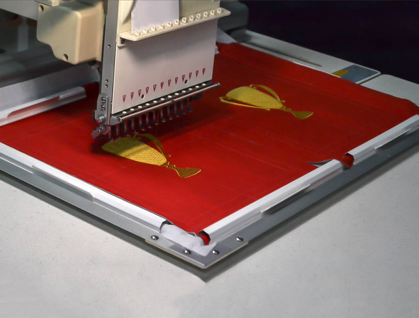 Industriële naaimachine voor borduurwerk maakt gouden bekers op een rode achtergrond - Foto, afbeelding