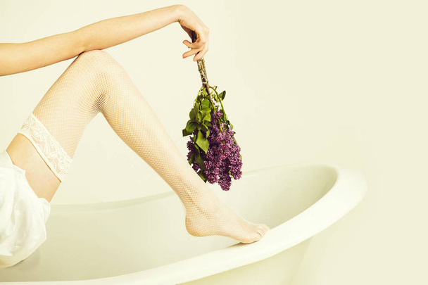 Aromatherapy, spa. Underwear fashion. lilac flower, leg in fishnet stocking and hand with bunch - Foto, Imagem