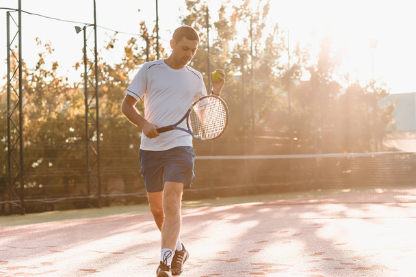  Un uomo che gioca a tennis al mattino alla luce del sole. Foto di un bel giovanotto sul campo da tennis. Un uomo che lancia palline da tennis. Area forestale come sfondo
 - Foto, immagini