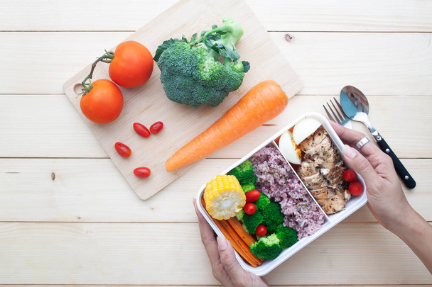 Vista superior das mãos da mulher segurando caixa de almoço saudável com peito de frango e legumes, comida saudável, refeição de nutrição
 - Foto, Imagem