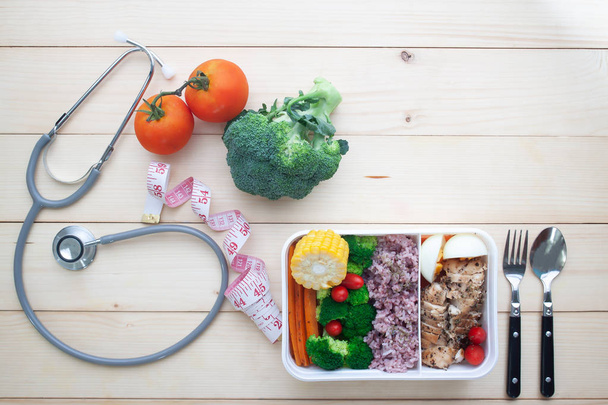 Creative flat lay of healthy concept, Stethoscope, measuring tape and chicken breast with vegetables lunch box on wooden background - Photo, Image