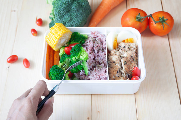 Рука женщины с помощью вилки едят здоровый обед коробка, гриль куриная грудка, вареное яйцо, рис и овощи
 - Фото, изображение