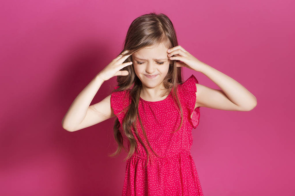 Pequena menina de 8 anos fazer algum gesto emocional com as mãos sobre um fundo neutro rosa. Ela tem cabelos longos morena e usar vestido de verão vermelho. Expressão engraçada em seu rosto
 - Foto, Imagem