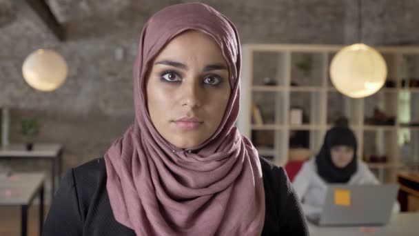 Portrait of young muslim women in hijab looking straight into camera, serious, two pretty womens working in modern office - Video