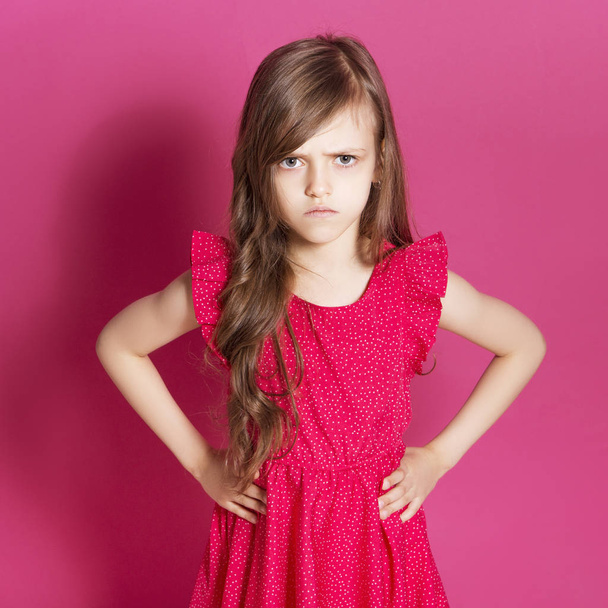 Petite fille de 8 ans faire un geste émotionnel avec ses mains sur un fond rose neutre. Elle a de longs cheveux bruns et porte une robe d'été rouge. Drôle d'expression sur son visage
 - Photo, image