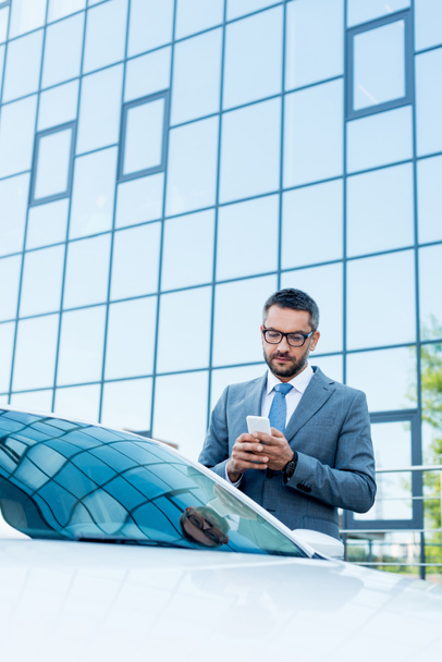 portrait of businessman using smartphone while standing at car on street - Foto, afbeelding