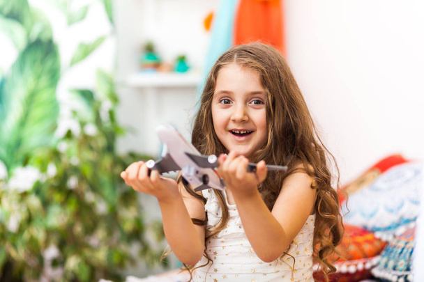 Charming little girl in cute arabic interior is holding an airplane. Travel concept. - Photo, Image