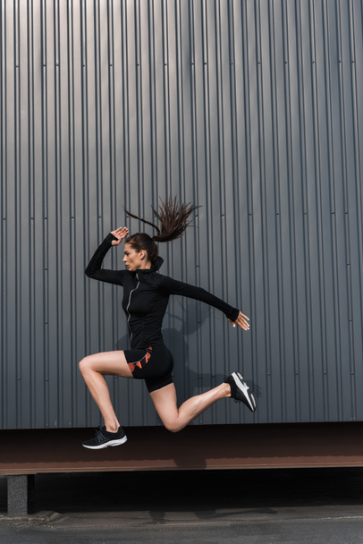 young sportswoman in black sportive thermal clothes jumping in city - 写真・画像