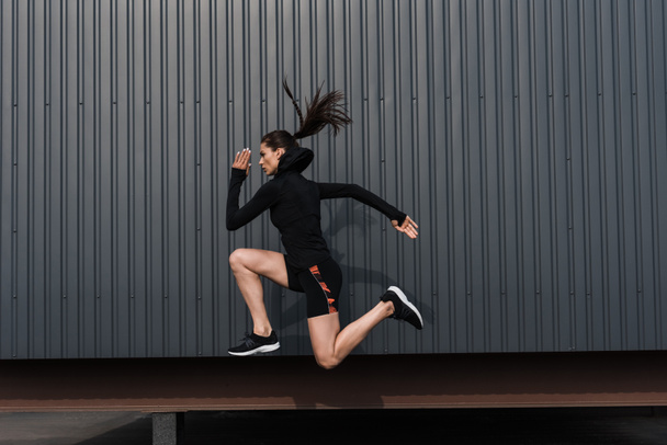 athletic woman in black thermal clothes jumping in city - Φωτογραφία, εικόνα