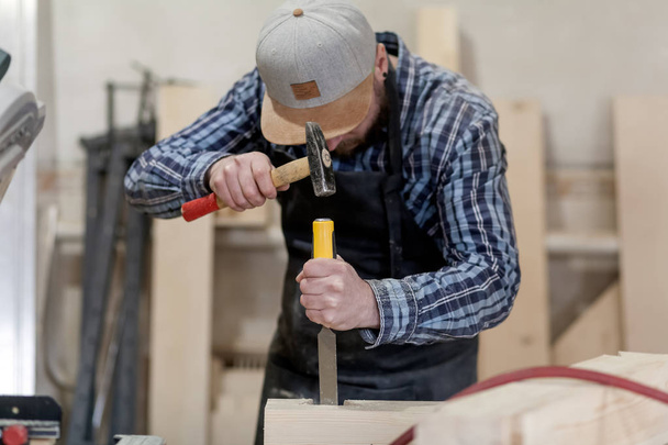 Ισχυρή ξυλουργός με ρούχα εργασίας σκάλισμα ξύλο χρησιμοποιώντας ένα εργαλείο επεξεργασίας ξύλου, σμίλη, χέρια εσωτερικη, ξυλουργική και δεξιοτεχνία έννοια - Φωτογραφία, εικόνα