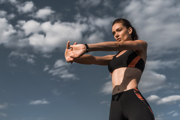 attractive sportswoman stretching hands against blue cloudy sky - Foto, Bild