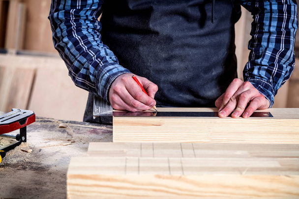 Κοντινό πλάνο Ο άνθρωπος μετρά μια ξύλινη σανίδα με χάρακα και μαρκάρει με μολύβι τα απαραίτητα σημεία για φέτες - Φωτογραφία, εικόνα