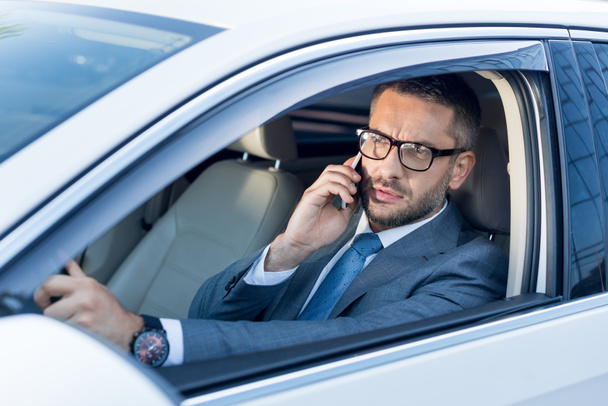 portrait of businessman in eyeglasses talking on smartphone while driving car  - Foto, imagen