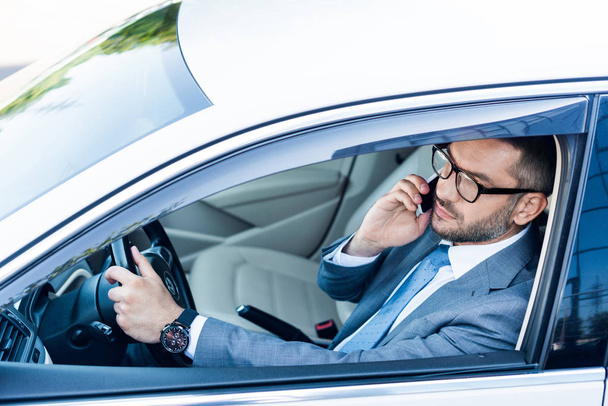 side view of businessman in eyeglasses talking on smartphone while driving car  - Foto, Imagem