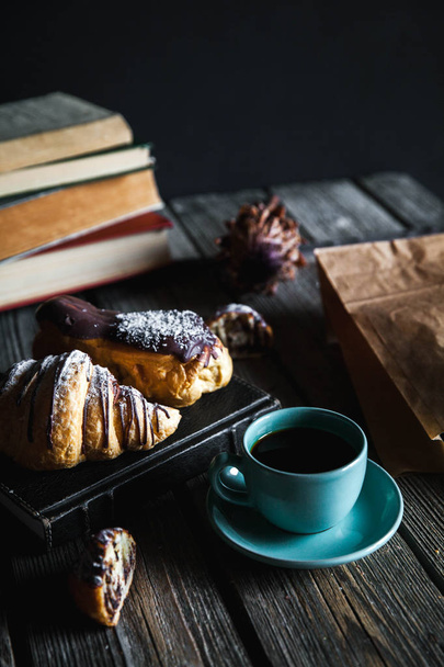 Croissant and white cup of black coffee on brown canvas. - Фото, изображение