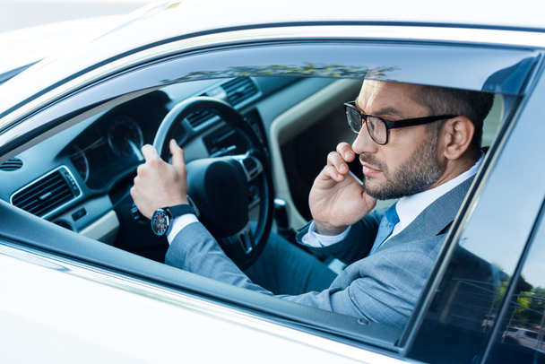 side view of businessman in eyeglasses talking on smartphone while driving car   - Фото, зображення