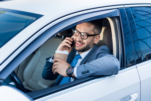 smiling businessman with coffee to go talking on smartphone in car  - Fotografie, Obrázek