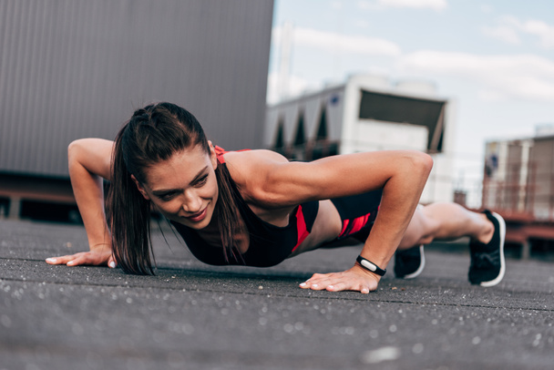 young smiling sportswoman doing push up on asphalt in city - Photo, Image