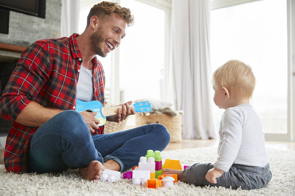 Father playing ukulele with young son at home - Foto, Bild