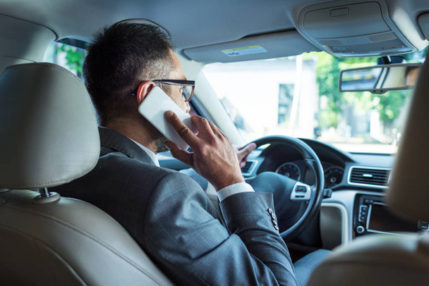vista trasera del hombre de negocios hablando en el teléfono inteligente mientras conduce el coche
  - Foto, imagen
