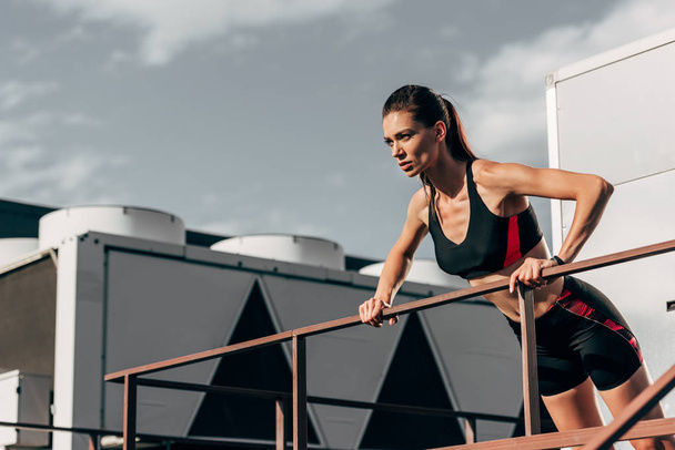 beautiful young sportswoman doing push up at railings on roof   - Photo, Image