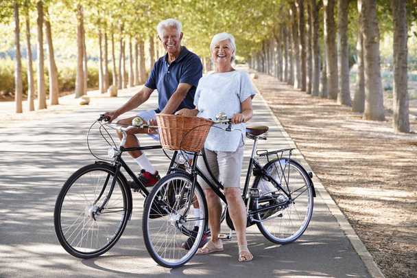 Portrait Of Smiling Senior Couple Cycling On Country Road - Fotó, kép