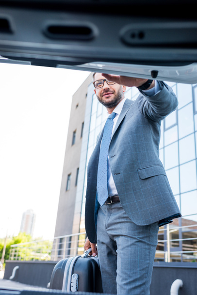 businessman in eyeglasses with luggage standing at car on parking - Foto, imagen