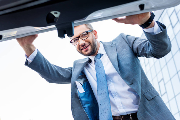 businessman in suit and eyeglasses looking into car luggage boot - Foto, imagen