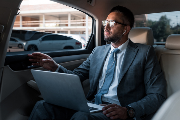 Geschäftsmann mit Kopfhörer und Laptop hört Musik im Auto - Foto, Bild