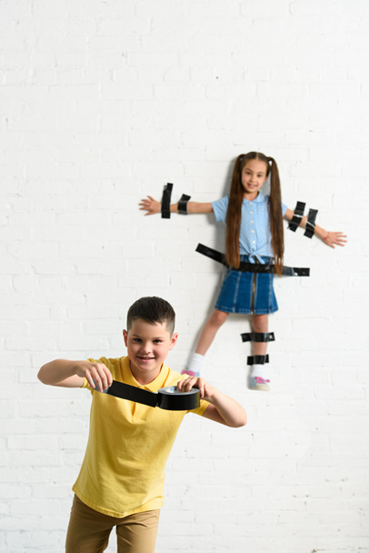 disobedient brother glued sister to wall with black tape at home - Fotografie, Obrázek