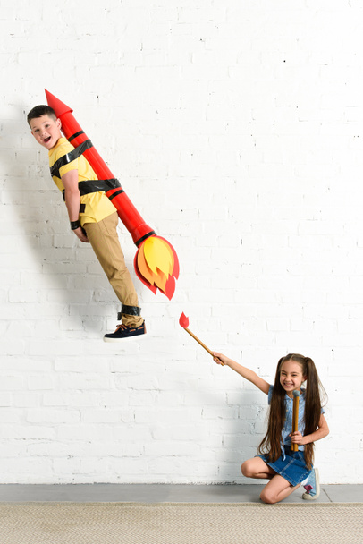 happy sister pretending setting on fire toy rocket with brother at home - Фото, изображение