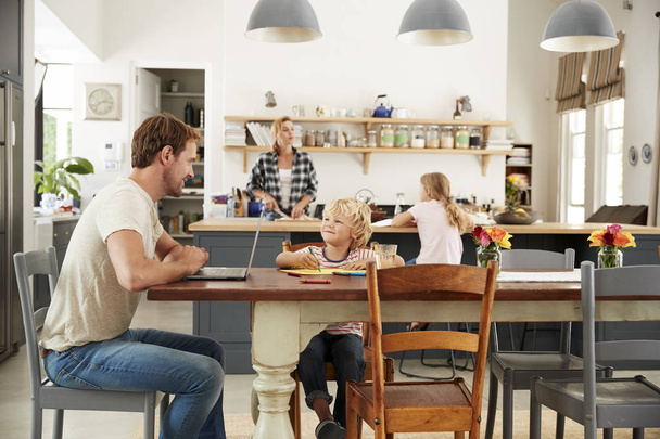 Baba ve oğul mutfak masası, anne ve kızı arka planda - Fotoğraf, Görsel
