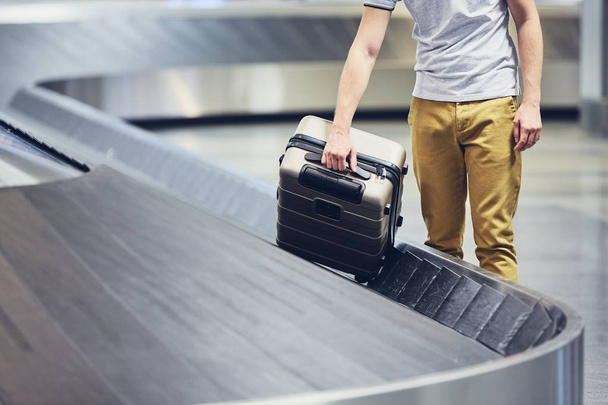 Man (traveler) picking up suitcase from baggage claim in airport terminal. - Fotó, kép