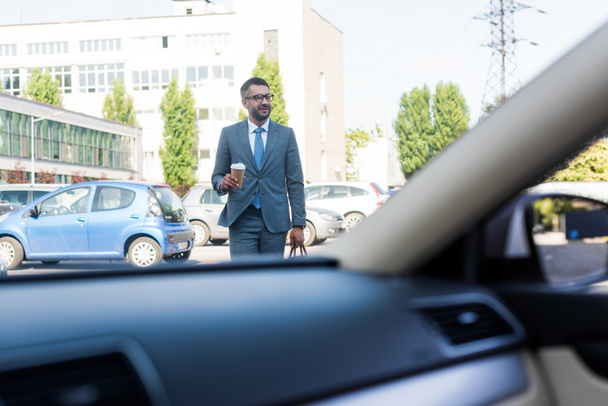 zakenman in pak en brillen met koffie te gaan gonna auto op straat - Foto, afbeelding