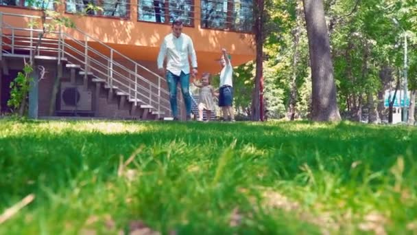 Father with his son and little daughter running along the green grass holding hands near the house - Materiał filmowy, wideo