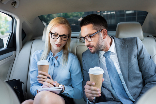 portrait of business people with coffee to go working on project on back seats in car - Photo, Image