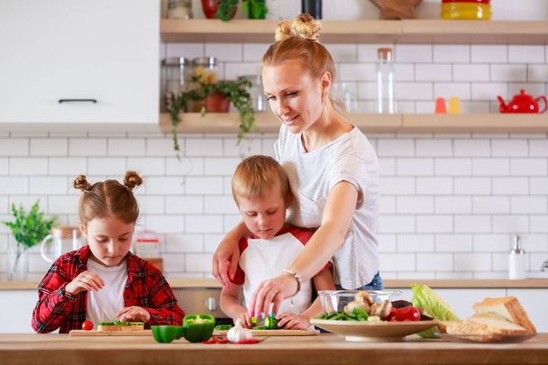 Foto de madre joven con hija e hijo cortando verduras en la mesa
 - Foto, imagen