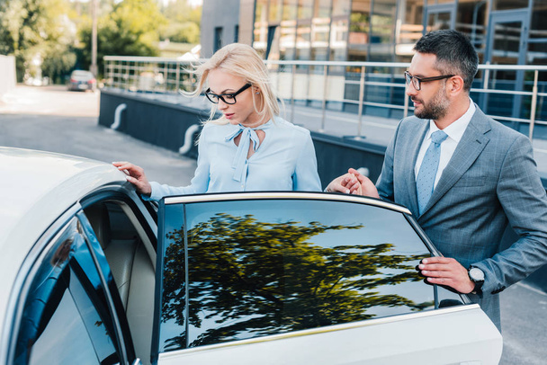 portrait of businessman helping colleague sit into car on street - Photo, Image