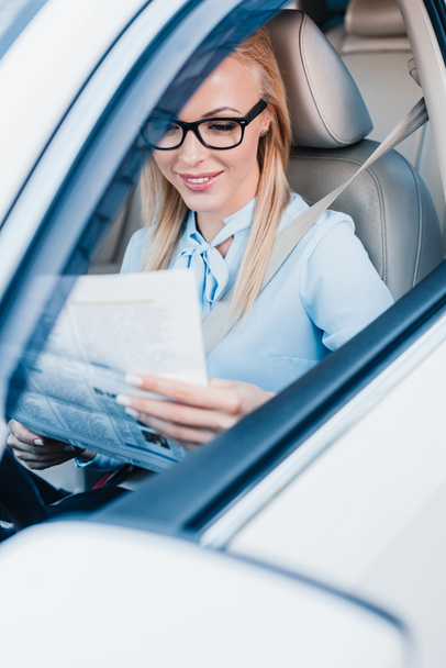 smiling businesswoman reading newspaper in car - Foto, afbeelding