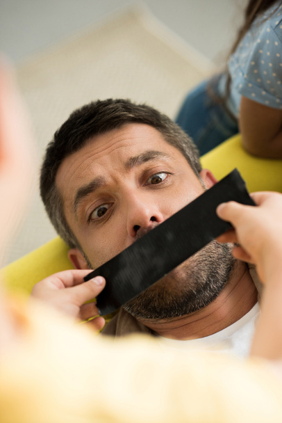 vysoký úhel pohledu dětí zavírání otec ústa s černou páskou doma - Fotografie, Obrázek