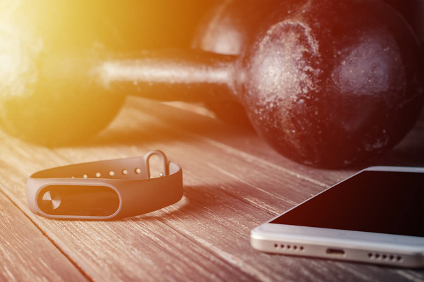 fitness tracker, smartphone and dumbbells on wooden background - Photo, Image