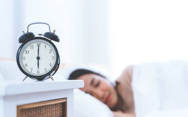 Alarm clock counting to six o clock with woman still sleeping in bed - Foto, afbeelding