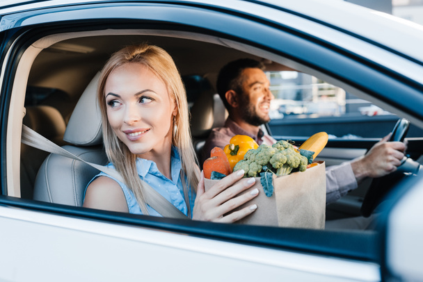 επιλεκτική εστίαση από παντρεμένο ζευγάρι με χάρτινη σακούλα γεμάτη από υγιεινά τρόφιμα στο αυτοκίνητο - Φωτογραφία, εικόνα