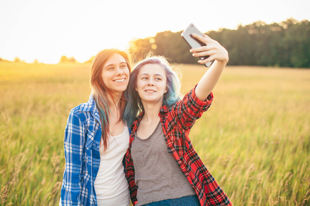 Two young women making selfie and standing on the field. Best friends - 写真・画像